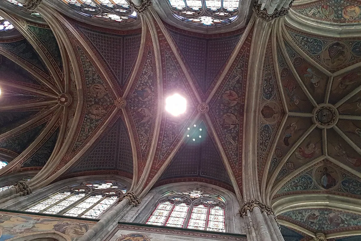 La volta stellata dipinta sopra il presbiterio della Votivkirche, con costoloni rossi, blu e dorati che si irradiano da una luce centrale.