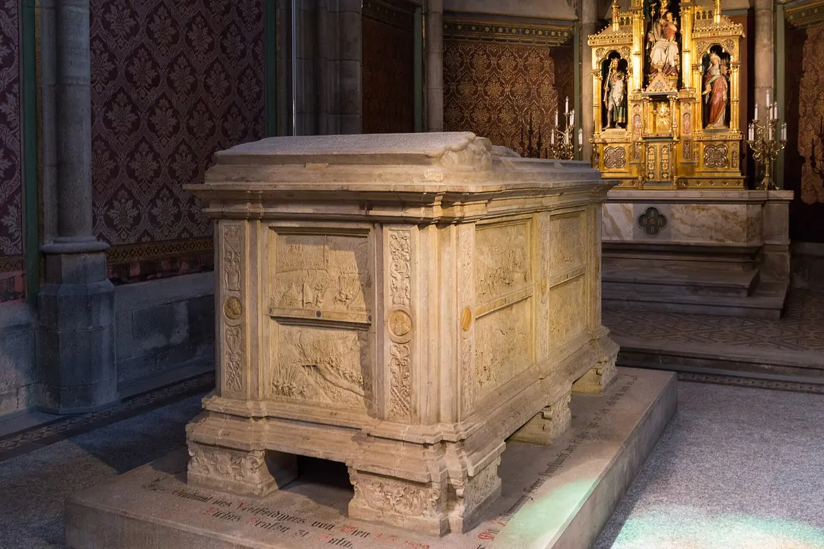 La tomba in arenaria del conte Nicola di Salm in una cappella laterale, con sculture in rilievo e un altare dorato sullo sfondo.